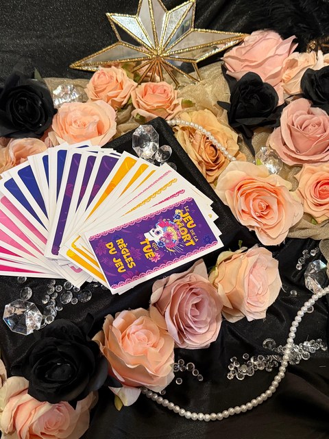 Cartes du jeu De la mort qui tue et livret de règles, mis en scène avec des roses et des bijoux
